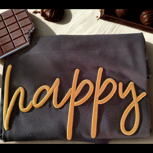 Gray tshirt with 'happy' embroidery surrounded by chocolate bars and truffles on a wooden surface