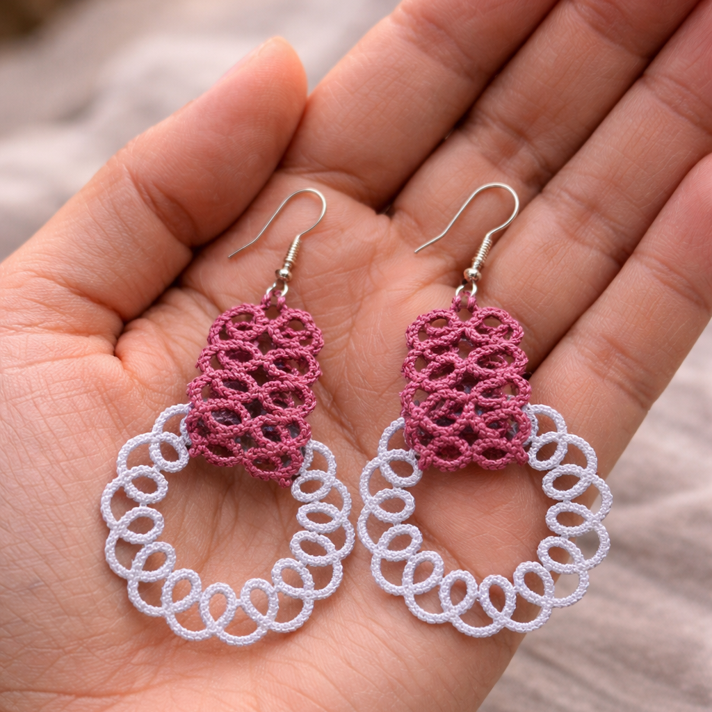 Pink and white earrings held in a hand against a neutral background