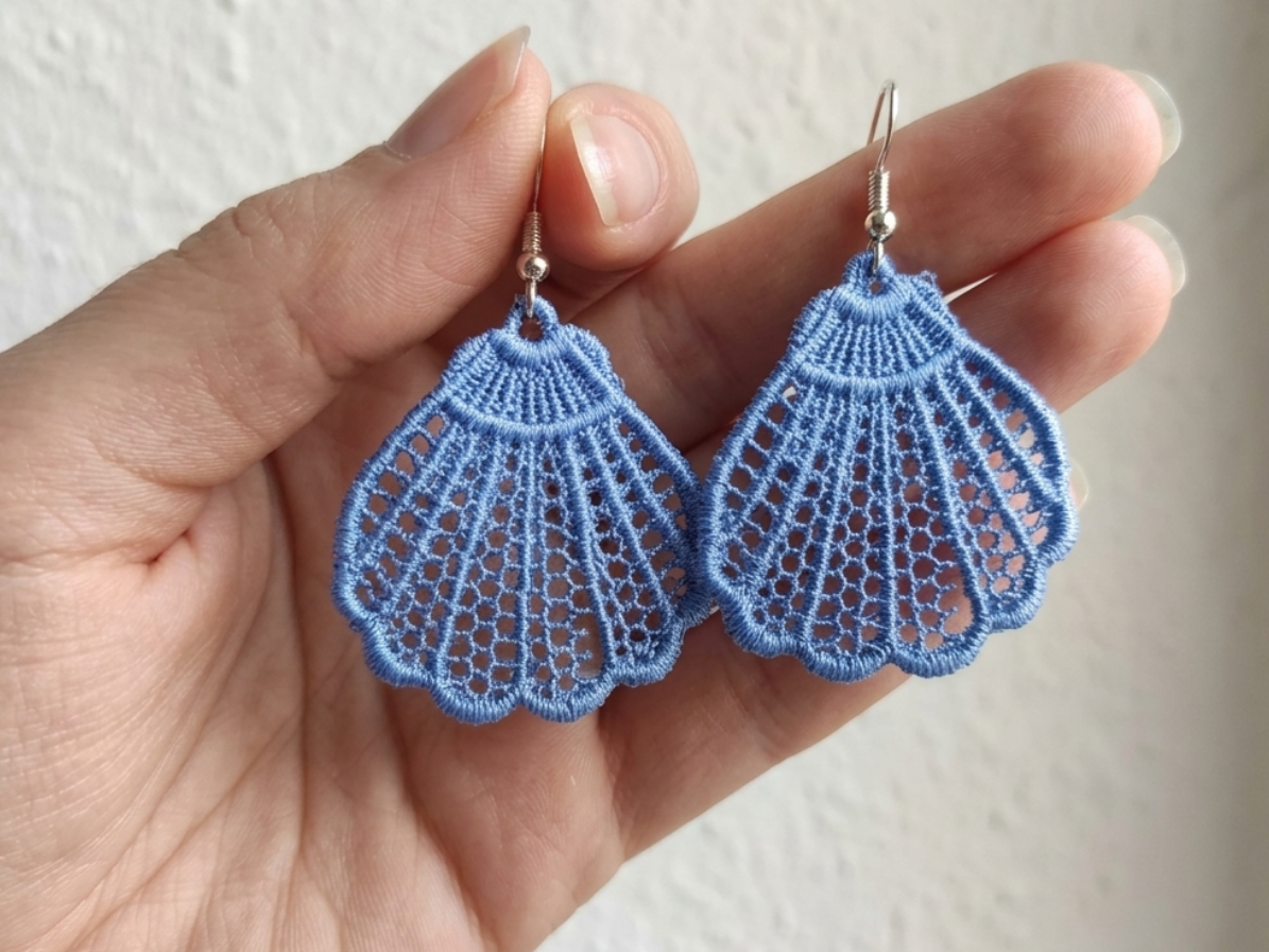 Blue lace earrings held in a hand against a neutral background