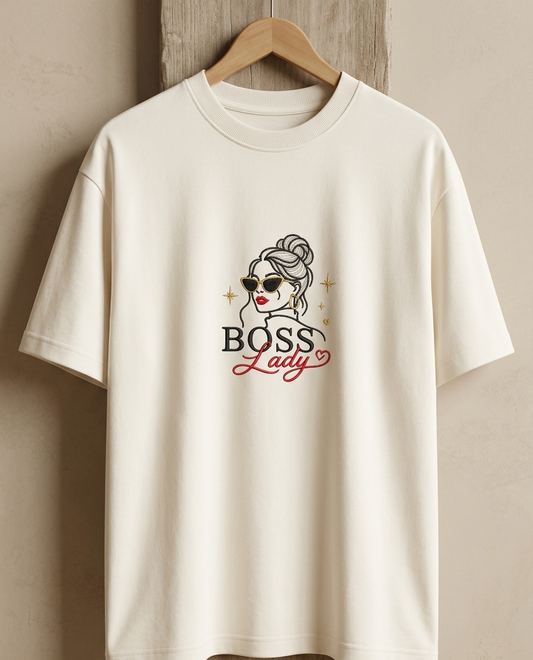 White t-shirt with 'Boss Lady' graphic on a wooden hanger against a beige wall.