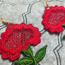 Red floral earrings with green leaves on a textured surface