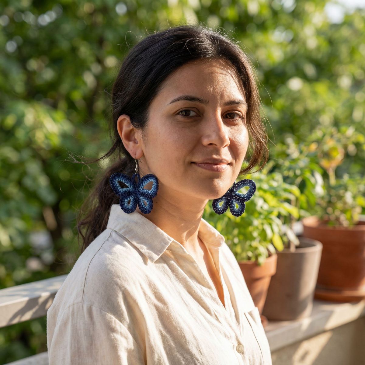 Woman wearing butterfly earrings outdoors with plants in the background