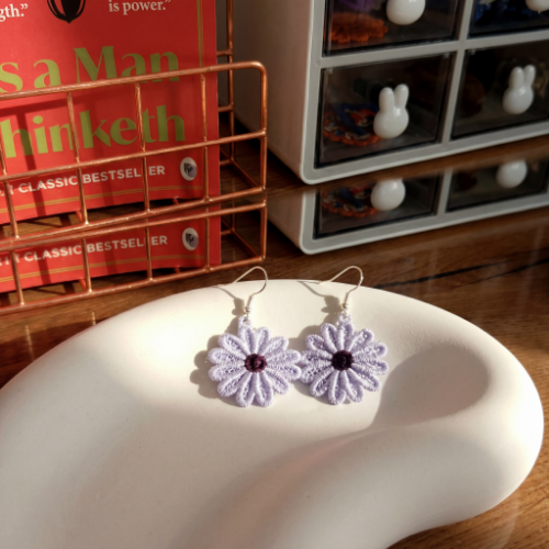 Flower-shaped earrings on a white surface with a bookshelf in the background