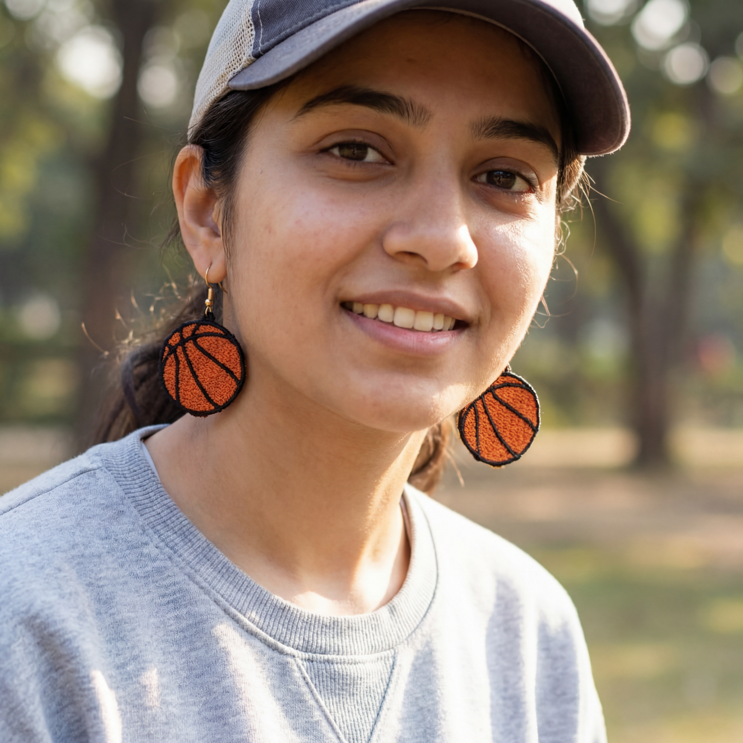 Woman wearing basketball-themed earrings and a cap in an outdoor setting