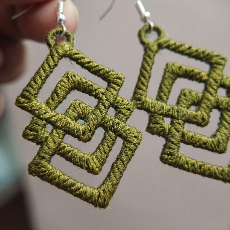 Green geometric earrings held by a hand against a neutral background