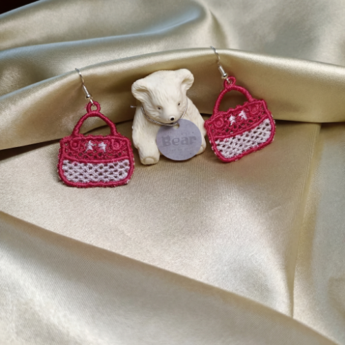 Pink and white handbag earrings with a small teddy bear on a satin surface