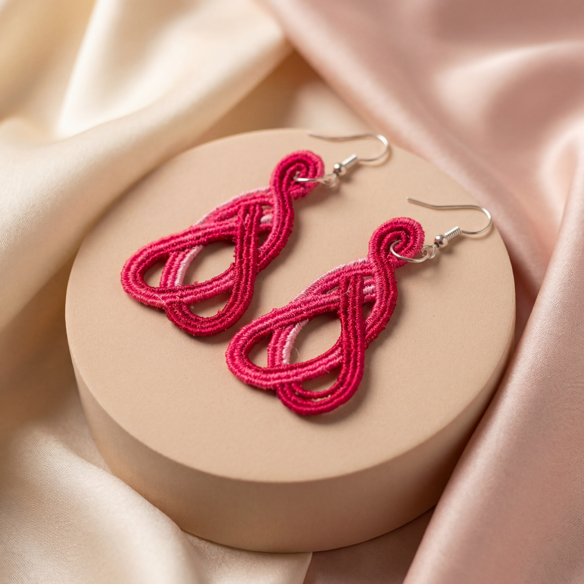 Pink earrings on a round beige platform with a soft pink fabric background