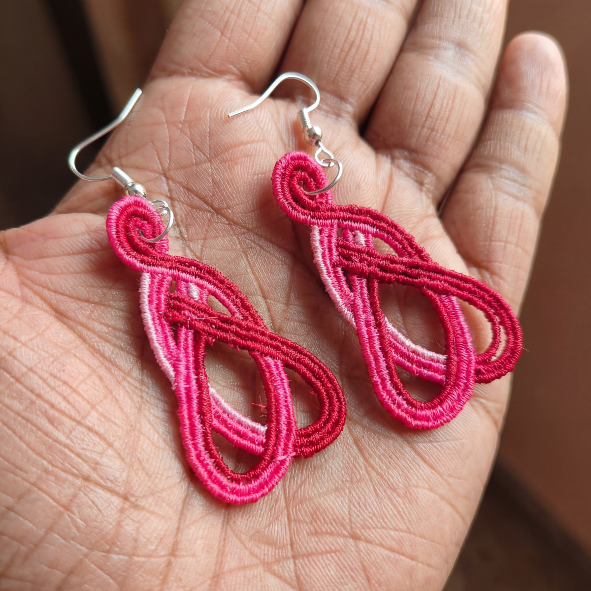 Pink embroidered earrings on a hand