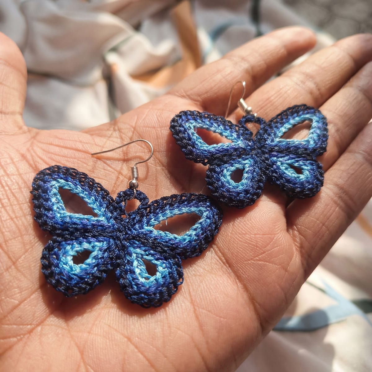 Blue butterfly earrings held in a hand with a blurred background