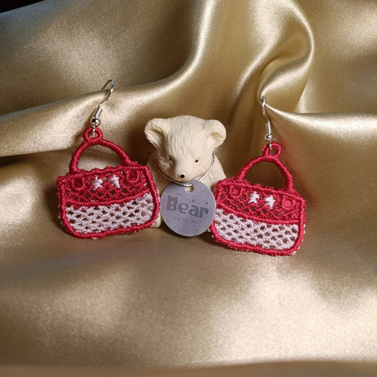 Red and white handbag earrings with a small bear figurine on a satin surface