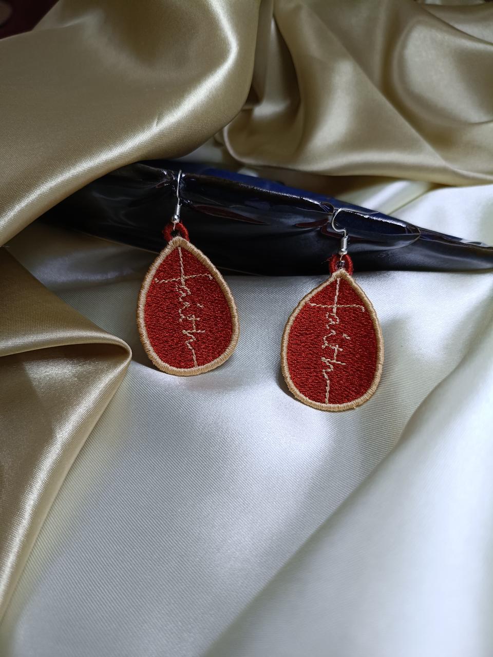 Teardrop-shaped earrings with red and gold design on a satin surface