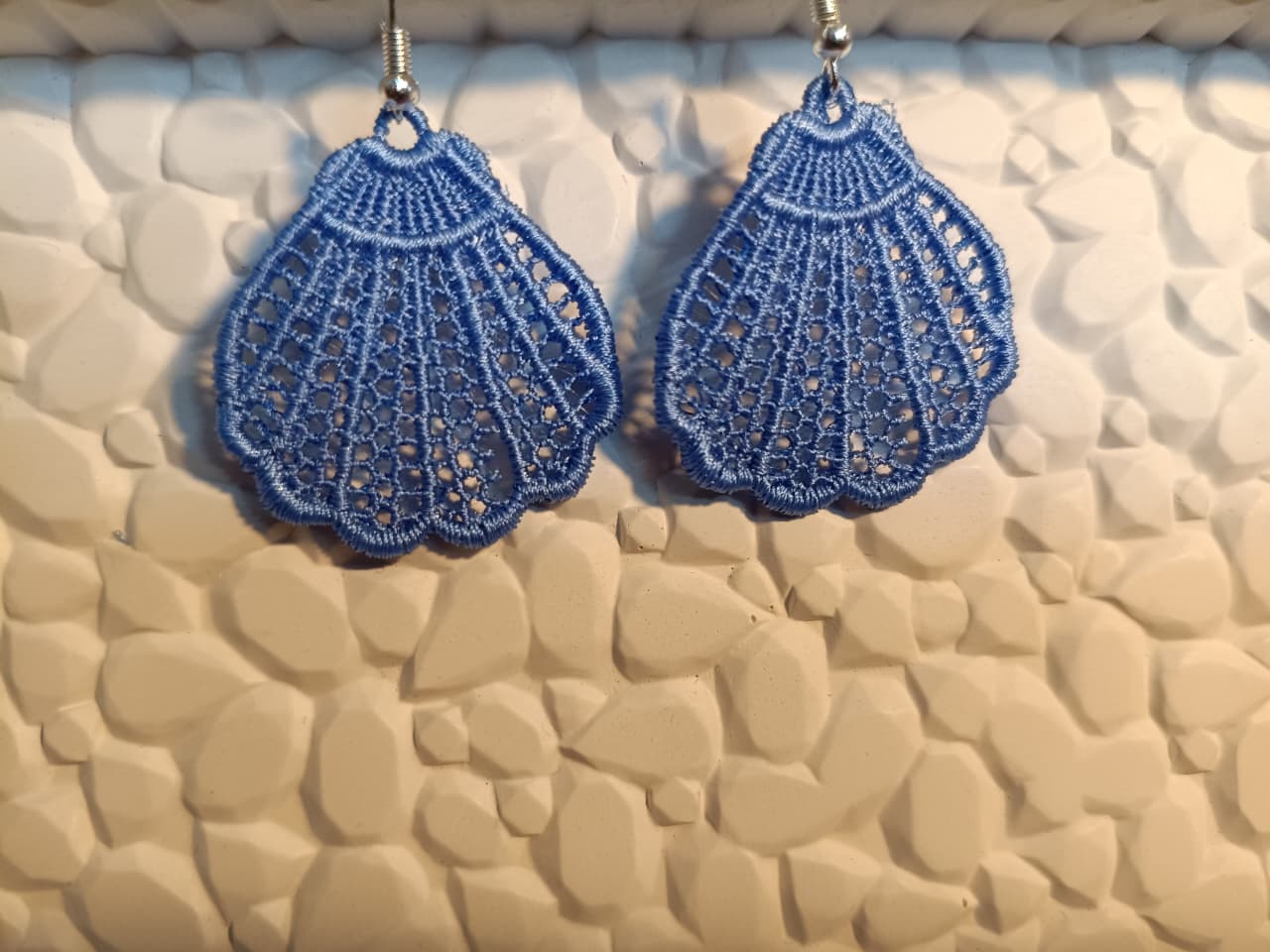 Blue lace earrings on a textured beige surface