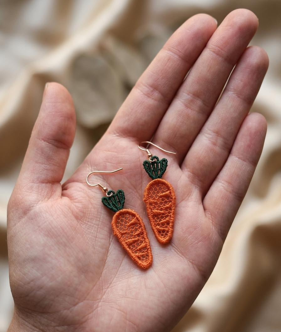 Carrot-shaped earrings held in a hand with a neutral background