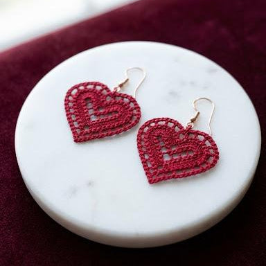 Red heart-shaped earrings on a white marble surface with a red fabric background