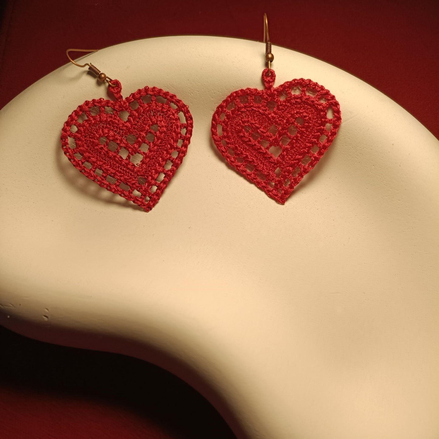 Red heart-shaped earrings on a beige stand with a red background