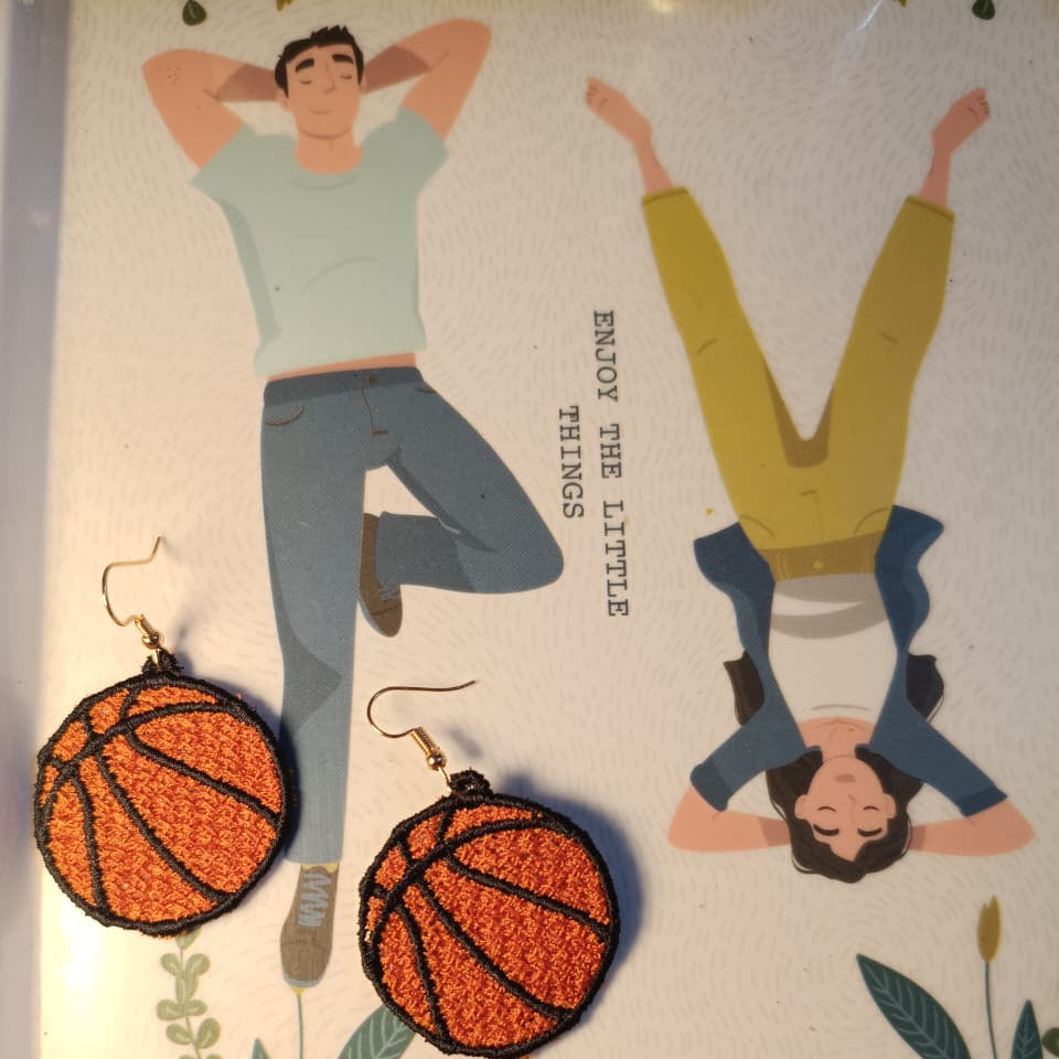 Basketball-shaped earrings on a decorative card with illustrations of people and plants.