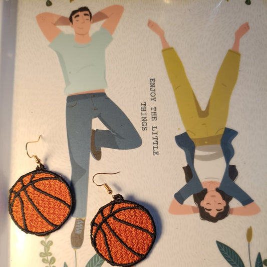 Basketball-shaped earrings on a decorative card with illustrations of people and plants.
