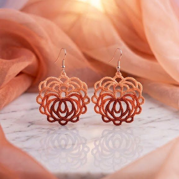 Rose gold floral earrings on a soft peach fabric background
