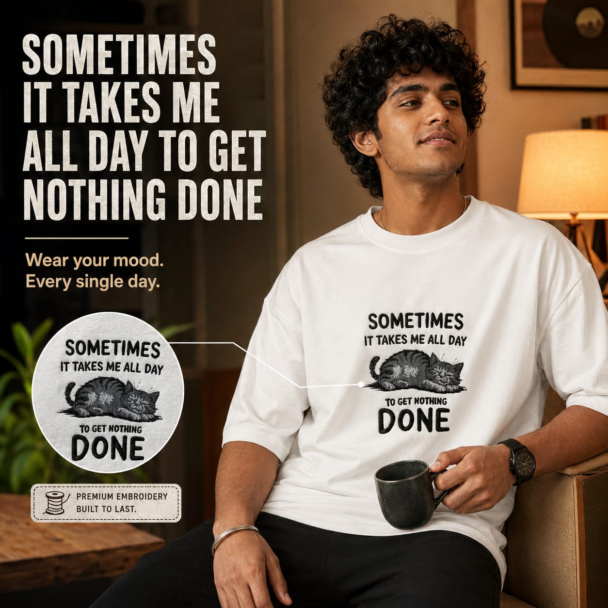 A man wearing a white crewneck t-shirt with a humorous black graphic print that reads 'SOMETIMES IT TAKES ME ALL DAY TO GET NOTHING DONE' with an illustration of a sleeping cat. The image is a promotional graphic with text overlays and a circular detail inset showing the premium embroidery texture.
