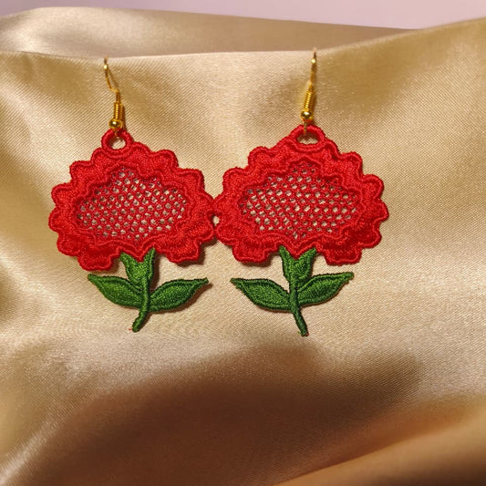 Red floral earrings with green leaves on a gold satin background