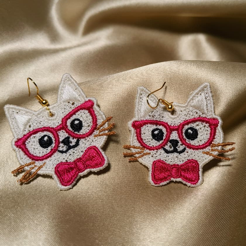 Cat-shaped earrings with pink glasses and bow ties on a satin background