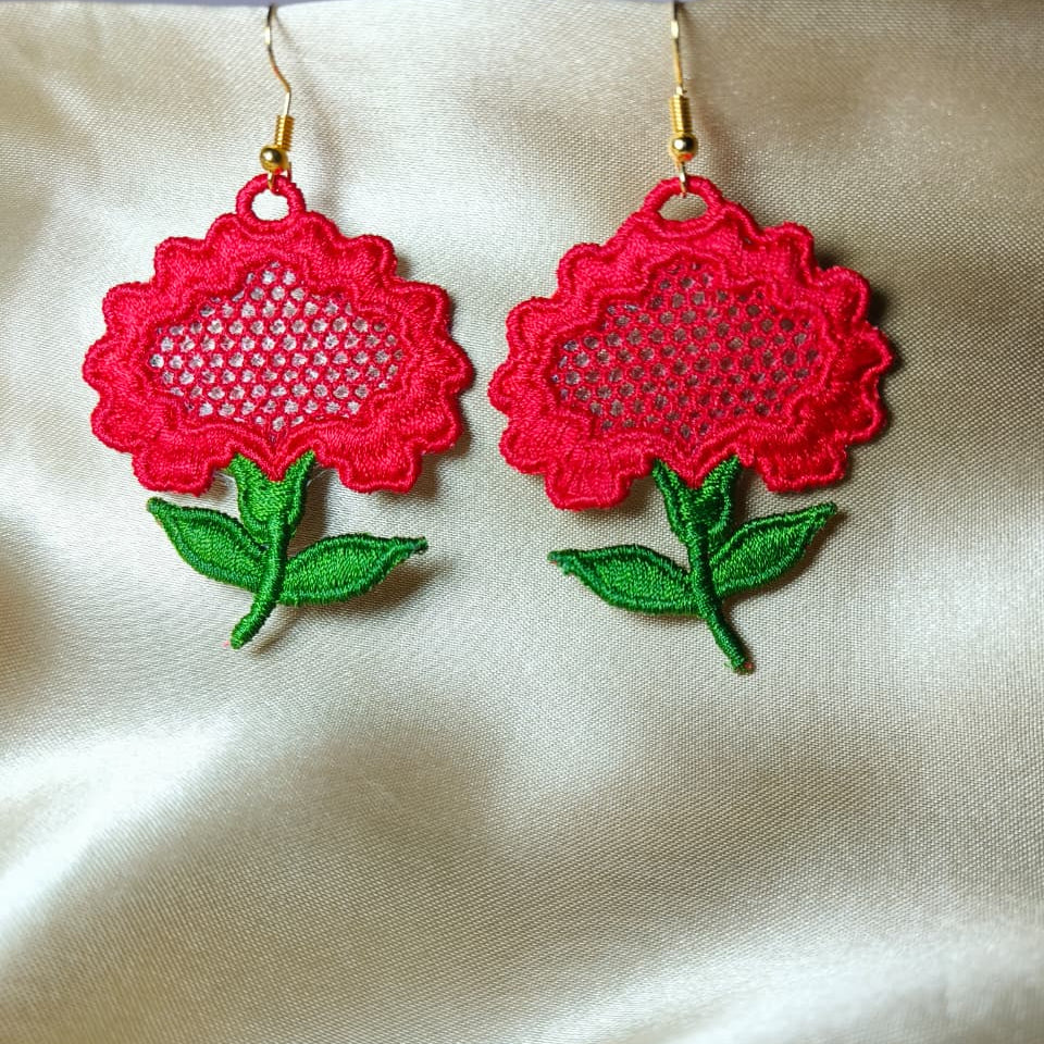 Red floral earrings with green leaves on a beige fabric background