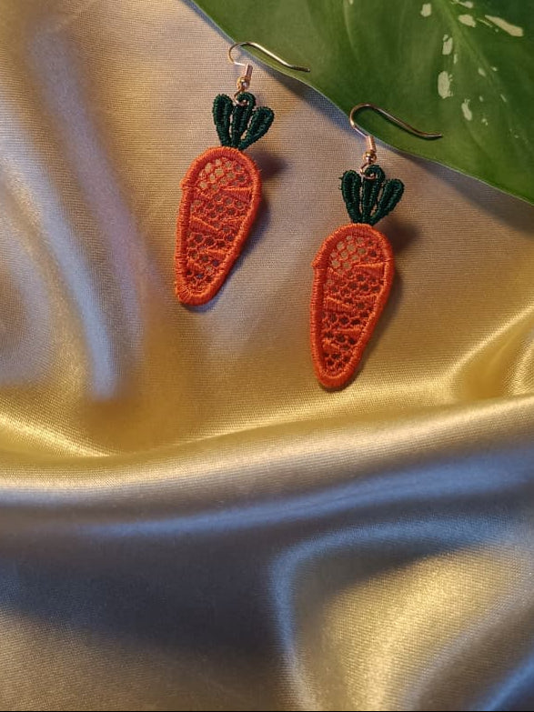 Carrot-shaped earrings on a satin surface with a leaf in the background