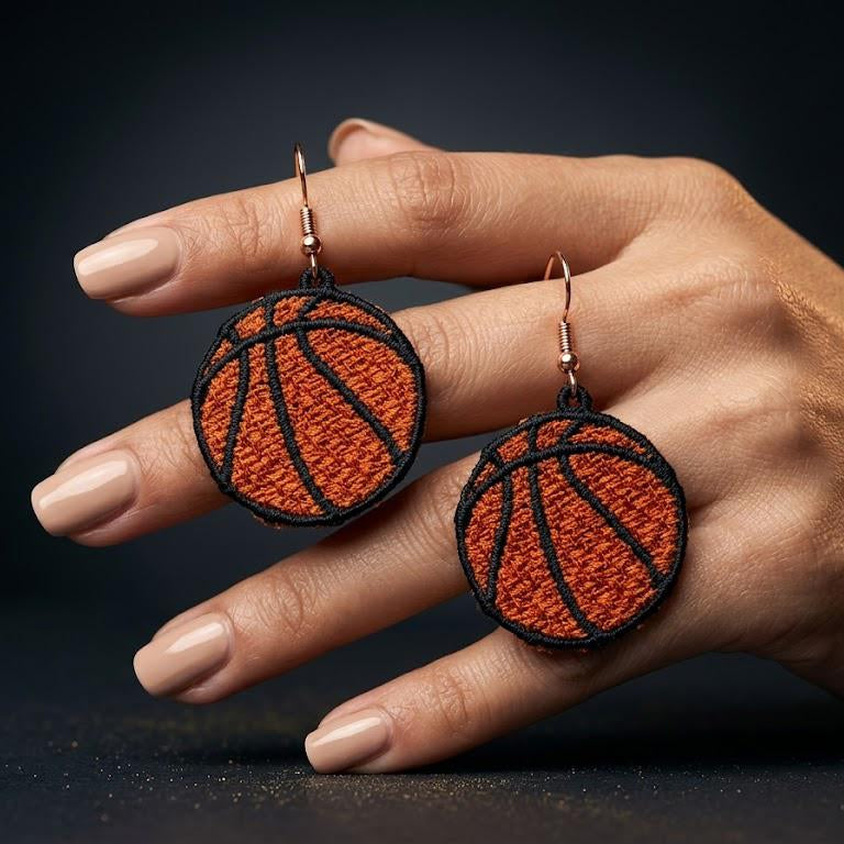 Basketball-themed earrings held in a hand against a dark background