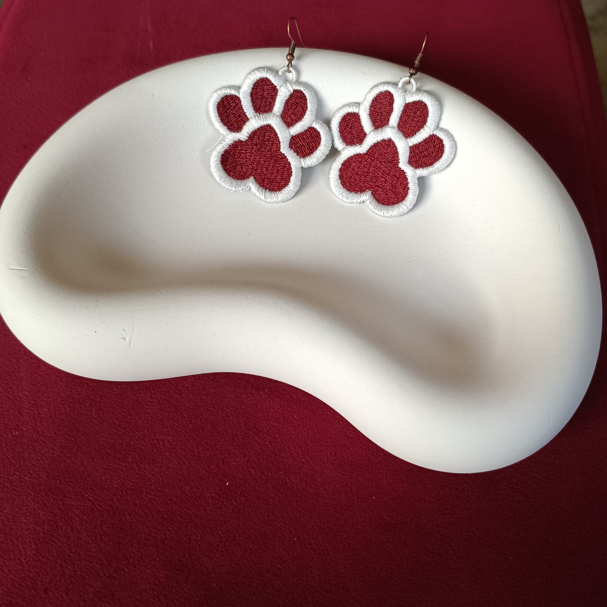 Red and white paw print earrings on a white dish with a red background